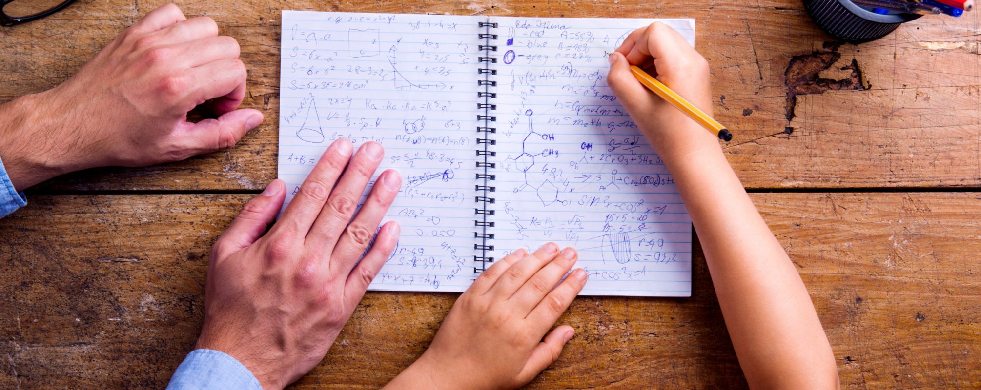 Unrecognizable father and son together, writing into notebook Unrecognizable father and son studying together, writing into a notebook. Studio shot on wooden background. Flat lay.