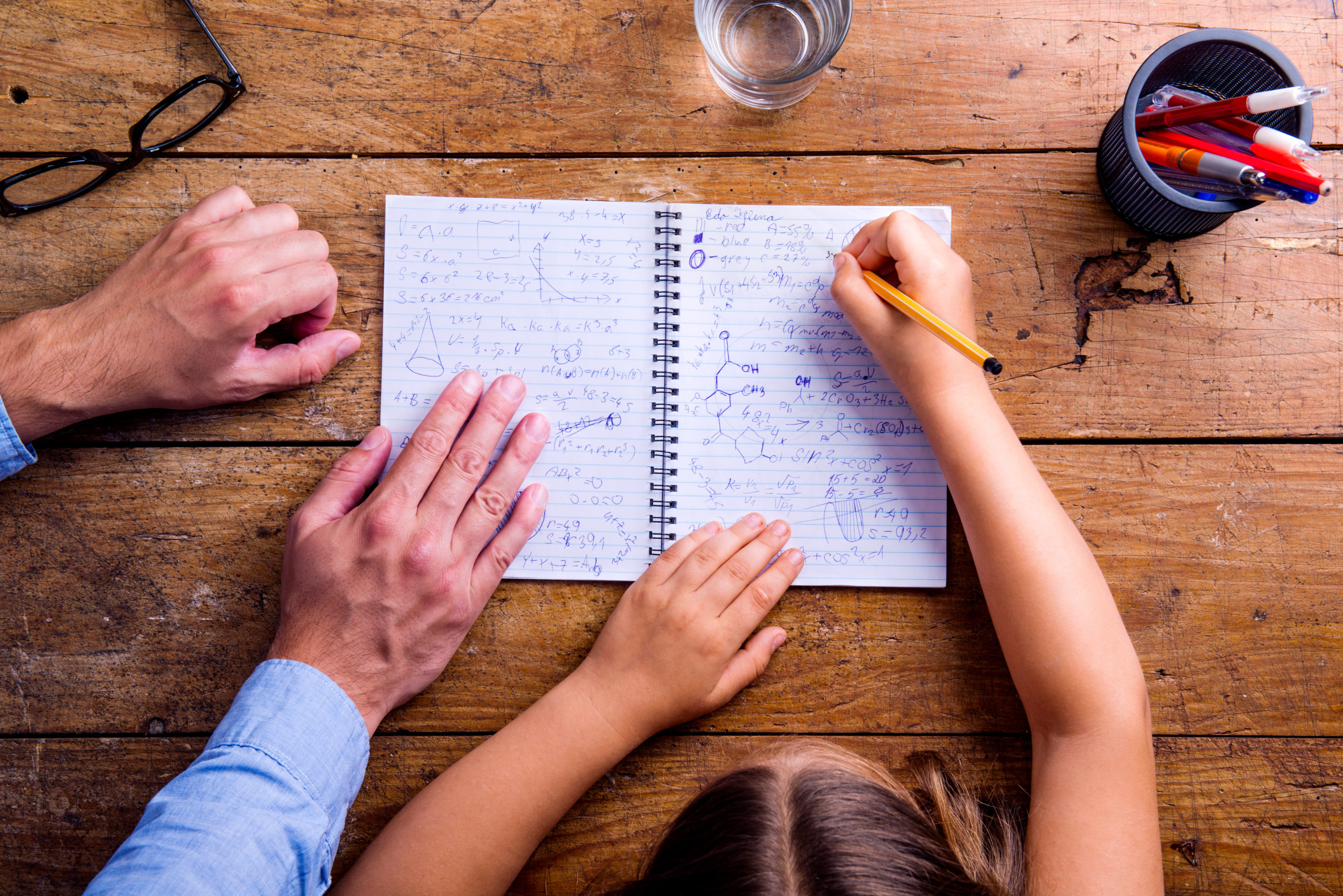 Unrecognizable father and son together, writing into notebook Unrecognizable father and son studying together, writing into a notebook. Studio shot on wooden background. Flat lay.